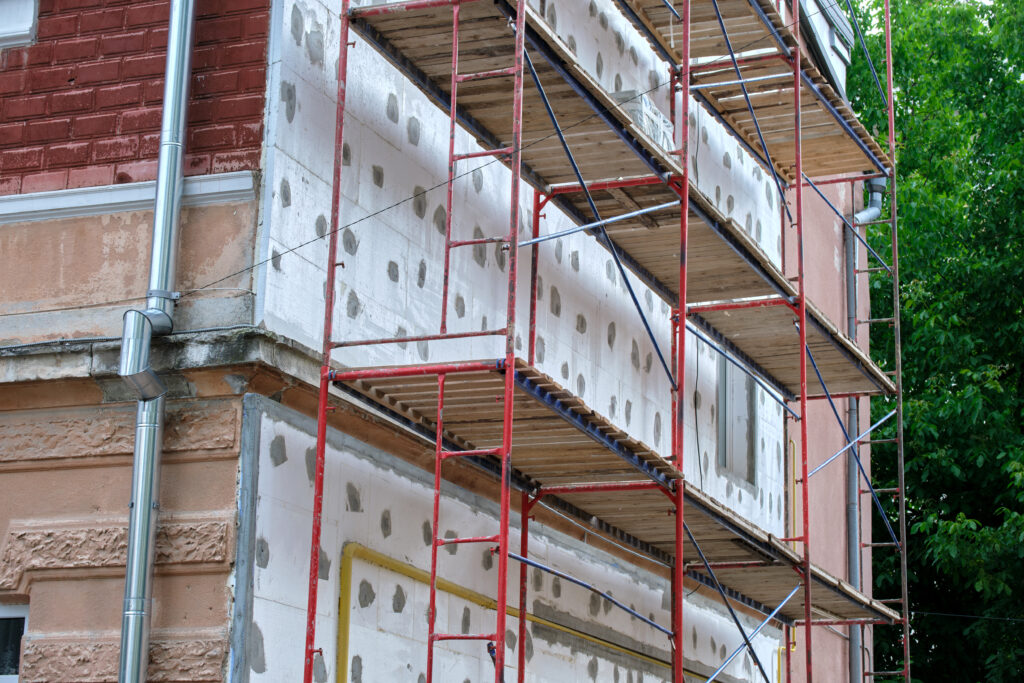 Échafaudage installé le long d’une façade en rénovation, avec panneaux isolants en polystyrène fixés sur les murs pour une isolation thermique par l’extérieur (ITE).