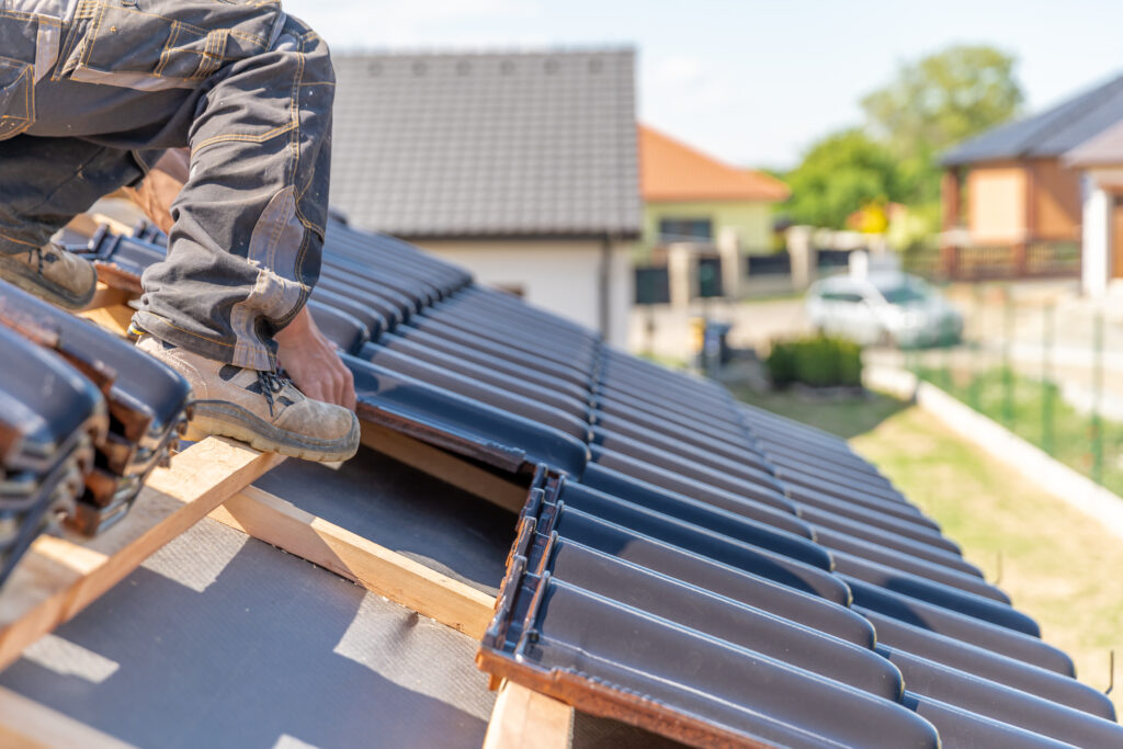 Ouvrier sur un toit en tuiles, installation et ajustement de tuiles et liteaux sur une toiture inclinée.