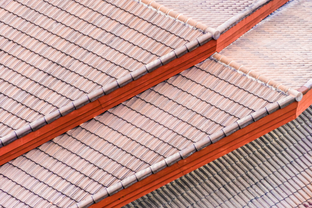 Vue en plongée d’une toiture en tuiles, avec plusieurs pans superposés séparés par des bandeaux rouges.